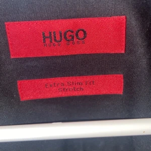 Svart skjorta Hugo Boss extra slim - Svart skjorta från Hugo Boss med extra slim fit och stretch. Klassisk krage, knäppning framtill och lång ärm. Perfekt för dig som gillar en stilren look.