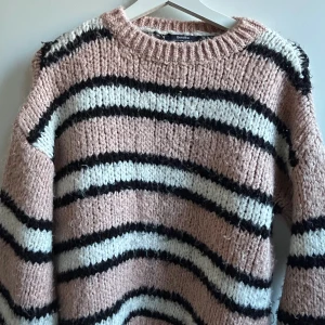 Randig stickad tröja från Bershka - Mysig stickad tröja från Bershka i ljusrosa med svarta och vita ränder. Tröjan har en chunky känsla, rund halsringning och långa ärmar. 