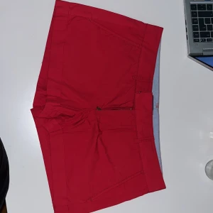 Röda shorts från Polo Jeans Ralph Lauren - Snygga röda shorts från Polo Jeans Company Ralph Lauren med broderad crest på bakfickan. Klassisk passform med dragkedja och bälteshällor. Tillverkade i bomull, perfekta för sommardagar. 