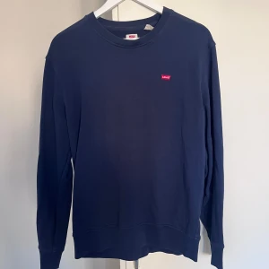 Mörkblå sweatshirt från Levi's - En stilren mörkblå sweatshirt från Levi's med klassisk rund hals och liten röd logotyp på bröstet. Tröjan har långa ärmar och är tillverkad i mjuk bomull, perfekt för en chill och enkel look.