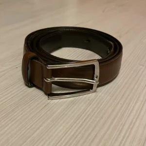 Brunt skärp  - Snyggt brunt bälte i skinn med klassiskt silverfärgat spänne. Perfekt accessoar från Jack and Jones i storlek 95. Skick 6/10. Skriv vid minsta fundering!