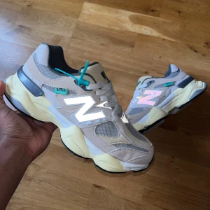 New Balance 9060 beige sneakers - Säljer ett par New Balance 9060 sneakers i beige och grått med vita och reflekterande detaljer. Skorna har chunky platt sula, mesh och mocka-paneler samt turkosa accenter. Ikonisk N-logga på sidan och snörning framtill. Perfekt för dig som gillar stilrena och trendiga sneakers.