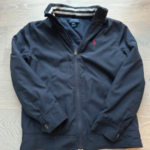 Svart vindjacka från Polo Ralph Lauren - Jag säljer min mörkblå vår/höstjacka eftersom den är för liten. Storlek M (10-12) år. Skick 9-10. Hör av dig vid minsta fundering🤔