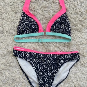 Mönstrad bikini  - Snygg oanvänd bikini från Yigga med svartvitt grafiskt mönster och detaljer i neonrosa och mintgrönt. Överdelen har triangelformade kupor och spänne i ryggen. Storleken skulle jag säga är runt en S