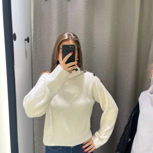 Vit stickad tröja med knappar H&M premium - Säljer en vit stickad tröja från H&M med coola svarta knappar längs axeln och kragen. Tröjan har en lite loose passform, ribbade muddar och lång ärm. Perfekt för dig som gillar stilrena detaljer och vill ha något mjukt och skönt till hösten.