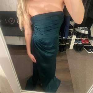 Mörkgrön axelbandslös långklänning - 🌸 säljer vidare denna klänning, köpt på PLICK (ordinarie pris 1799kr) 🌸 endast använd en gång (av personen jag köpte den av), inga defekter 🌸 normal i storleken 🌸 ser mer grön ut i verkligheten än på bilderna 🌸 slits, dragkedja där bak och silikon remsor vid bysten 🌸 klänningen är ca 140cm lång och midjemåttet ca 34cm (jag som har på mig klänningen är 159cm lång)