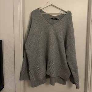 Grå stickad v-ringad tröja Bik Bok - Mysig grå stickad tröja från Bik Bok med v-ringning och ribbade muddar. Tröjan har en loose passform och långa ärmar, perfekt för lager på lager under kyliga dagar.