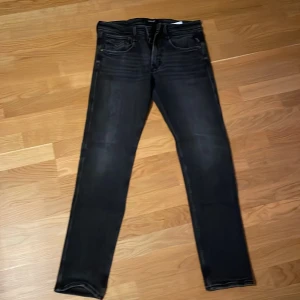 Svarta Replay Anbass jeans 31/32 - Svarta Replay Anbass jeans med snyggt tvättad look och klassiska fem fickor. Jeansen har smal passform och raka ben, tillverkade i stretchigt jeanstyg för extra komfort. Perfekta för dig som gillar en stilren och modern vibe.