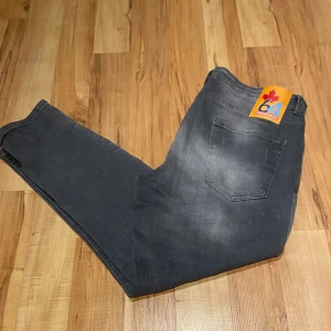 Svarta Dsquared2 jeans med slitningar - Säljer ett par svarta Dsquared2 jeans med coola slitningar och färgstänk framtill. Jeansen har klassisk femficksdesign, Dsquared2-logga på bakfickan och röd etikett vid fickan. Snyggt tvättade för en trendig look och tillverkade i jeansmaterial.
