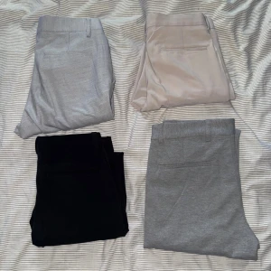 Fyra par kostymbyxor i olika färger - Säljer fyra par stilrena kostymbyxor i svart, ljusgrått, mörkgrått och beige. Byxorna har raka ben, hällor för bälte och bakfickor. Perfekta för en dressad look och passar till skjorta eller t-shirt.       1. Ljusgråa kostymbyxor från ASOS storlek 28/32 2. Beiga kostymbyxor från ASOS storlek 28/30 3. Svarta kostymbyxor från ASOS storlek 28/32 4. Ljusgråa finbyxor från Lindbergh, slim fit cropped length, uppvikta. Vet inte storlek  