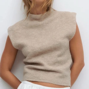 Beige stickad ärmlös topp - Helt oanvänd. Mysig beige stickad topp med hög hals och ärmlös design. Perfekt för lager-på-lager och har en enkel, stilren look som passar till många outfits. Mjuk och skön känsla tack vare det stickade materialet.