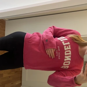 Rosa stickad tröja från Bondelid - Säljer en rosa stickad tröja från Bondelid med vit broderad text på bröstet. Tröjan har rund halsringning, ribbade muddar och är långärmad. Perfekt för dig som gillar en klassisk och chill stil.