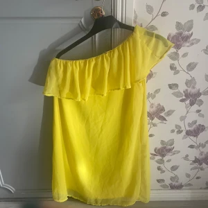 Gul offshoulder klänning med volang - Superfin gul klänning med offshoulder och bred volang upptill. Lätt och luftig modell som ger en riktigt somrig vibe. Perfekt för dig som gillar färg och vill sticka ut. Klänningen är kort och har en lös passform som känns bekväm hela dagen.