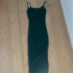 Mörkgrön långklänning från Amisu - Snygg mörkgrön långklänning från Amisu med smala axelband och figurnära passform. Klänningen har en enkel, stilren design och är perfekt för dig som gillar minimalistisk stil. Materialet känns mjukt och följsamt mot kroppen.