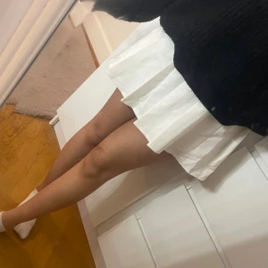 Vit plisserad kortkjol - Säljer en vit plisserad kortkjol med klassisk A-linjeform. Kjolen har tydliga veck och är gjord i ett mjukt bomullsmaterial som känns bekvämt mot huden. Perfekt för dig som gillar en clean och fräsch stil med lite preppy vibe.