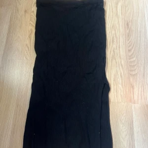Svart ribbad långkjol från H&M - Svart långkjol från H&M Basics i ribbat material. Kjolen har en rak och tight passform som sitter snyggt längs kroppen. Perfekt för dig som gillar en stilren och enkel look. Midjemodell utan synliga detaljer.