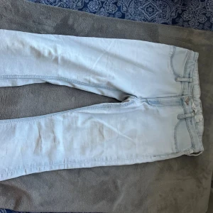 Ljusblåa jeans från H&M low waist - Säljer ett par ljusblåa jeans från H&M med låg midja och justerbar midja. Klassisk femficksmodell i mjukt denimtyg, perfekt för en avslappnad stil. Passar dig som gillar en enkel och clean look.