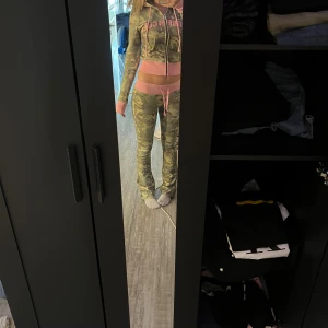 Camo sett från Hidden Cult - Säljer ett par låga cargopants från Hidden Cult i camomönster med breda rosa ribbade muddar och snörning i midjan. Byxorna har en tight passform och coola rosa detaljer, samt broderad text bak. Även en tröja matchande till Perfekt för dig som vill sticka ut.