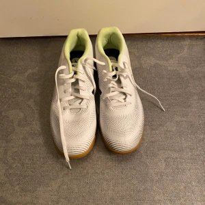 Vita sneakers från Puma med gummisula - Säljer ett par fräscha vita sneakers från Puma med svart logga på sidan och häl. Skorna har snörning, ventilerande meshmaterial och ljusgult foder. Sulan är i gummi och ger bra grepp. Perfekta för träning eller häng med kompisar.Helt nya och oanvända 