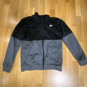 Svart och grå ziptröja från Adidas - Snygg ziptröja från Adidas i svart och grått med klassisk logga på bröstet. Tröjan har hel dragkedja, ståkrage och två fickor framtill. Perfekt för träning eller chill. Tillverkad i mjukt och smidigt polyestermaterial.