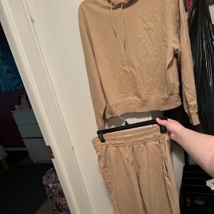 Beige set Hoodie och mjukisbyxor med snörning strl: L - Säljer ett beiget set mjukisbyxor med luvtröja med snörning i midjan och bekväma sidofickor. Byxorna har en loose passform och är gjorda i mjukt bomullsmaterial, perfekta för chill dagar hemma eller när du vill vara extra comfy.