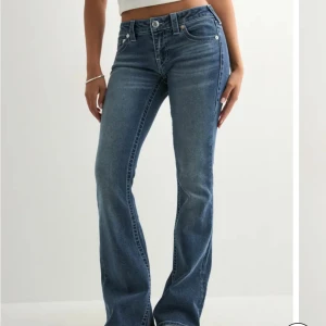 Blå bootcut jeans från True Religion - Snygga blå jeans från True Religion med klassiska kontrastsömmar och ikoniska bakfickor. Modellen har bootcut-ben och låg midja, tillverkade i stretchig denim för en bekväm passform. Perfekta för dig som gillar en tidlös och cool look.