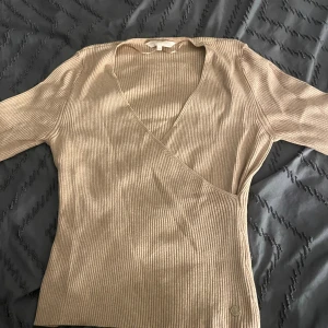 Beige tröja - En beige tröja med en V linje vid bröstet och en design plus en liten detalj på framsidan vid tröjan där nere perfekt för vardagen 