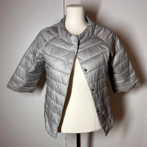 Trekvartsärmad jacka / dunjacka  - Trendig trekvartsärmad dunjacka i grå. Storlek s. Perfekt till hösten över en stickad tröja Fint skick förutom två mindre defekter som visas på de sista bilderna. Därav det billigare priset.  