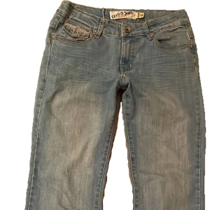 Blå bootcut jeans från Seyoo Jeans - Snygga ljusblå jeans från Seyoo Jeans med bootcut passform. Jeansen har broderade detaljer på bakfickorna och klassisk femficksdesign. Tillverkade i jeansmaterial med slitningar framtill för en cool look. Jeansen är originellt storlek L men insydda så passar som mindre❣️ Är själv 170 lång och byxorna är smått korta