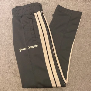 Palm Angels byxor - Palm Angels träningsbyxor i färgen mörkgrå med beige ränder längs sidorna. Väldigt sällsynt färg! Skick: 9/10 storlek: S. Nypris: 3000kr Vid fler frågor/bilder är det bara och höra av sig.