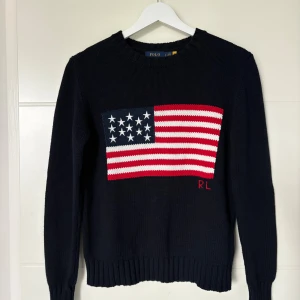 Mörkblå stickad tröja Polo Ralph Lauren - Snygg mörkblå stickad tröja från Polo Ralph Lauren med amerikansk flagga framtill och RL-broderi. Tröjan har rund halsringning, ribbade muddar och är långärmad. Står storlek S men jag tycker passformen är mer som XS. Hör av er vid minsta fundering! Priset är inte hugget i sten!