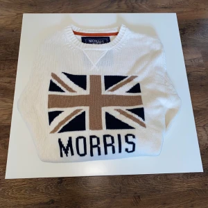 Vit stickad tröja Morris med flagga - Säljer en snygg stickad tröja från Morris i cremevitt med det ikoniska brittiska flaggmotivet i beige och marinblått på bröstet. Tröjan är i mycket fint skick – använd sparsamt och väl omhändertagen.  Detaljer: 	•	Märke: Morris 	•	Färg: Cremevit med beige och marinblå detaljer 	•	Storlek: M 	:Passform: Normal 	•	Skick: Mycket gott skick, inga fläckar eller hål  En perfekt tröja för höst och vår 