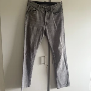 Grå jeans från Jack & Jones 29/32 - Snygga grå jeans från Jack & Jones i klassisk rak modell. Jeansen har fem fickor, bälteshällor och en stilren tvättad look. Perfekta för dig som gillar en enkel och clean stil. Materialet är mjukt och bekvämt bomullsjeans.