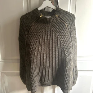 Stickad khaki poncho från Hunkydory - Säljer en chunky stickad poncho från Hunkydory i khaki färg. Tröjan har grov ribbstickning, högt krage och två snygga guldfärgade dragkedjor vid halsen. Perfekt för dig som gillar en cool och avslappnad stil. Går att dra upp på sidorna med dragkedjor💓💓