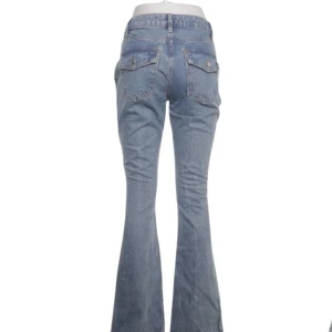 Lågmidjade Bootcut jeans  - Ljusblå lågmidjade/ mid waist bootcut jeans från ASOS Design. Femficksmodell med knappar där bak. Midjemått 74cm. Ger 2000 tal känsla, inga defekter