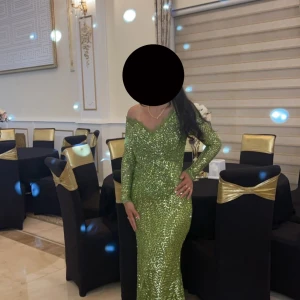 Grön glittrig långklänning - Säljer en elegant grön långklänning med glittriga paljetter och offshoulder-skärning. Klänningen har långärmade ärmar och figurnära passform, perfekt för dig som vill sticka ut på festen. Snygg v-ringning och vackert mönster i paljetterna.