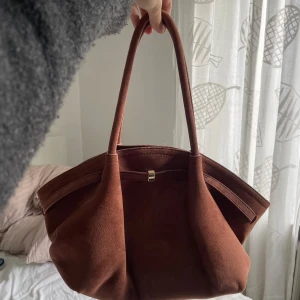 Brun handväska i mocka-imitation - Snygg och rymlig handväska i brun mocka-imitation. Perfekt skick och inga defekter, bara använt några gånger!