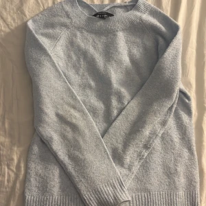 Ljusblå stickad tröja från Vero Moda - Supermjuk ljusblå stickad tröja från Vero Moda med rund halsringning och ribbade muddar vid ärmslut och nederkant. Perfekt för lager-på-lager och chill dagar. Enkel och stilren design som är lätt att matcha.