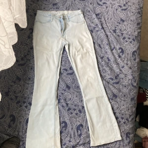 Ljusblå utsvängda jeans från H&M - Säljer ett par ljusblå jeans från H&M med utsvängda ben och låg midja. Jeansen har justerbar midja och klassisk femficksdesign. Perfekta för dig som gillar retrovibbar och vill ha en snygg siluett.