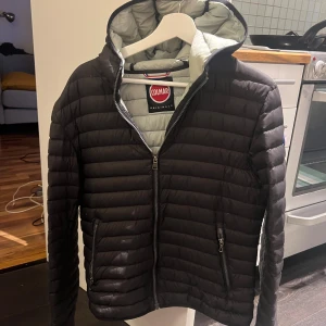 Svart pufferjacka från Colmar - Snygg svart pufferjacka från Colmar med huva och quiltad design. Jackan har dragkedja framtill och på fickorna, samt Colmar-logga på ärmen. Insidan är ljusgrå och materialet är lätt och smidigt, perfekt för kyliga dagar. Storlek 48 skick 8/10 , perfekt nu till höst och vinter.       Priset är ej hugget i sten :)