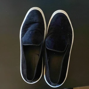 Limitato svarta slip-on sneakers 42 - Svarta slip-on sneakers från Limitato med vit platt sula och rund tå. Ovandelen är i mjuk mocka som ger en lyxig känsla och snygg textur. Tillverkade i Italien, stilrena och enkla att dra på. Perfekta för dig som gillar minimalistisk design. 42