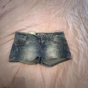Low waist jeansshorts  - Snygga blå low waist jeansshorts med slitna detaljer och nitar längs fickorna.