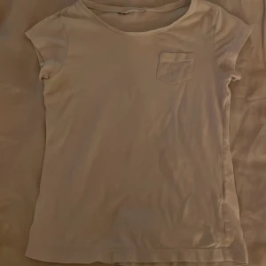 Beige kortärmad t-shirt med ficka - En basic beige t-shirt med korta ärmar och en liten bröstficka på vänster sida. T-shirten har rund halsringning och är tillverkad i ett mjukt material som känns skönt mot huden. Perfekt för en avslappnad och enkel stil. Skjortan är ungefär xxs!!!!!!!