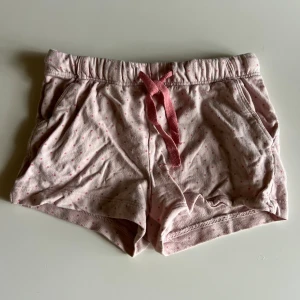 Rosa prickiga shorts från H&M - Söta ljusrosa shorts från H&M med små rosa prickar och en bred resår i midjan. De har en rosa snörning framtill och är gjorda i mjuk bomull, perfekta för varma dagar. Avslappnad passform och två fickor på sidorna.