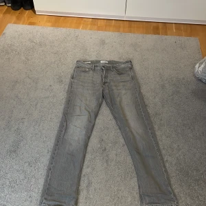 Gråa relaxed jeans från Jack & Jones - Säljer ett par gråa jeans från Jack & Jones, modell Relaxed/Chris. Jeansen har en avslappnad passform med raka ben och klassisk femficksdesign. Tillverkade i denim med snygg tvättad look och detaljerade sömmar. Perfekta för en chill och stilren vibe.
