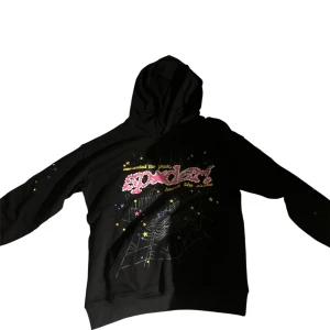 Svart hoodie med tryck från SP5DER - Svart hoodie från SP5DER med färgglatt tryck framtill, spindelnätsmotiv och stjärnor. Tröjan har huva och långa ärmar, perfekt för dig som gillar streetwear med unik design.
