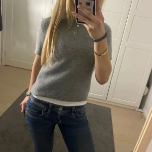 Grå stickad kortärmad tröja - Mysig grå stickad tröja med korta ärmar och rund hals. Tröjan har en enkel och stilren design, perfekt att matcha med jeans eller kjol. Ribbstickade kanter ger en snygg detalj och den är superbekväm att bära.