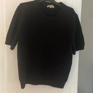 Svart stickad tröja från H&M - En svart stickad tröja från H&M med rund halsringning och korta ärmar. Tröjan har en enkel och clean look, perfekt att styla med jeans eller kjol. Mjuk och skön känsla tack vare det stickade materialet.