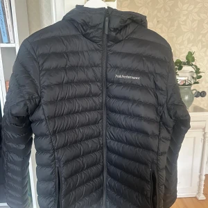 Mörkblåa dunjacka Peak Performance - Mörblå dunjacka från Peak Performance med huva och dragkedja framtill. Den är använd men i väldigt fint skick.