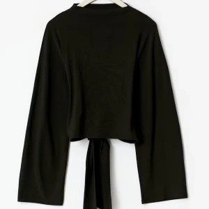 Svart croppad topp med knytband - Svart croppad topp med långa vida ärmar och snyggt knytband i ryggen. Toppen har en enkel och stilren design som passar perfekt till jeans eller kjol. Materialet känns mjukt och följsamt mot huden. Toppen är nästintill aldrig använd. Nypris 300 